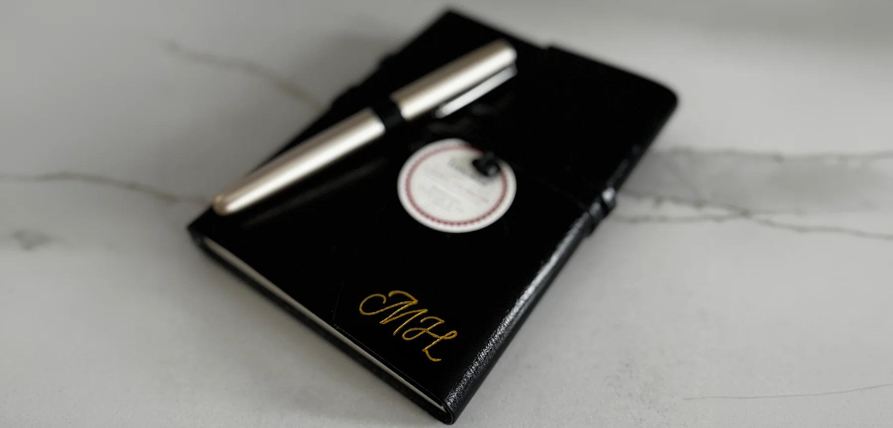 Gold foiling on a black keepsake book beside a calligraphy pen